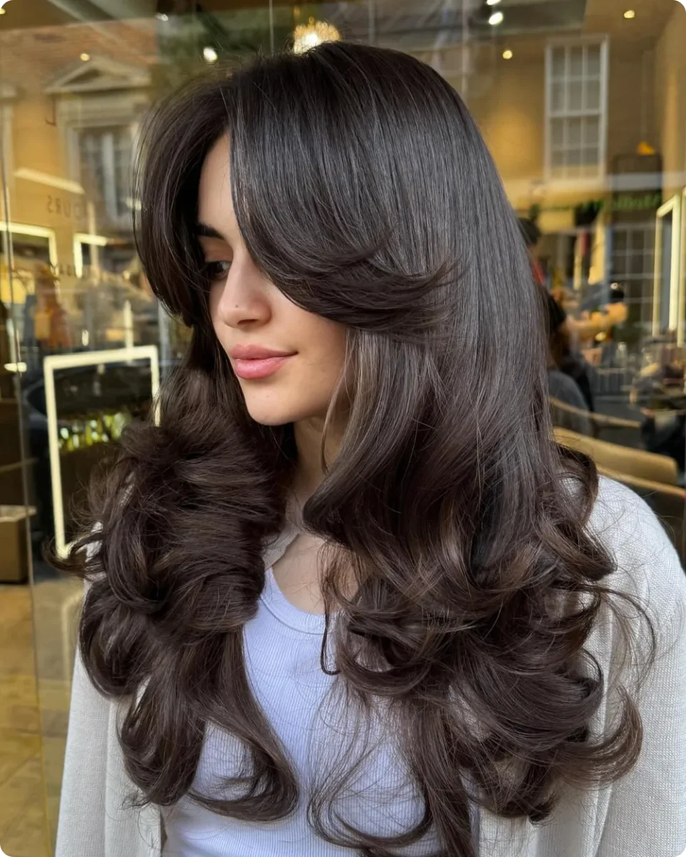 Dark brown blowout with a soft swoop across the forehead and rolled curls at the ends