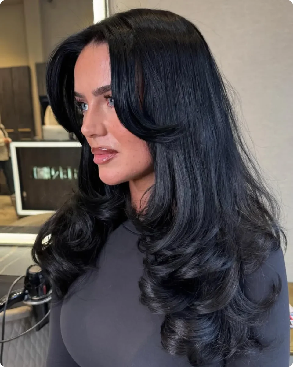 Deep side part on long black hair with smooth roots and thick barrel curls at the ends