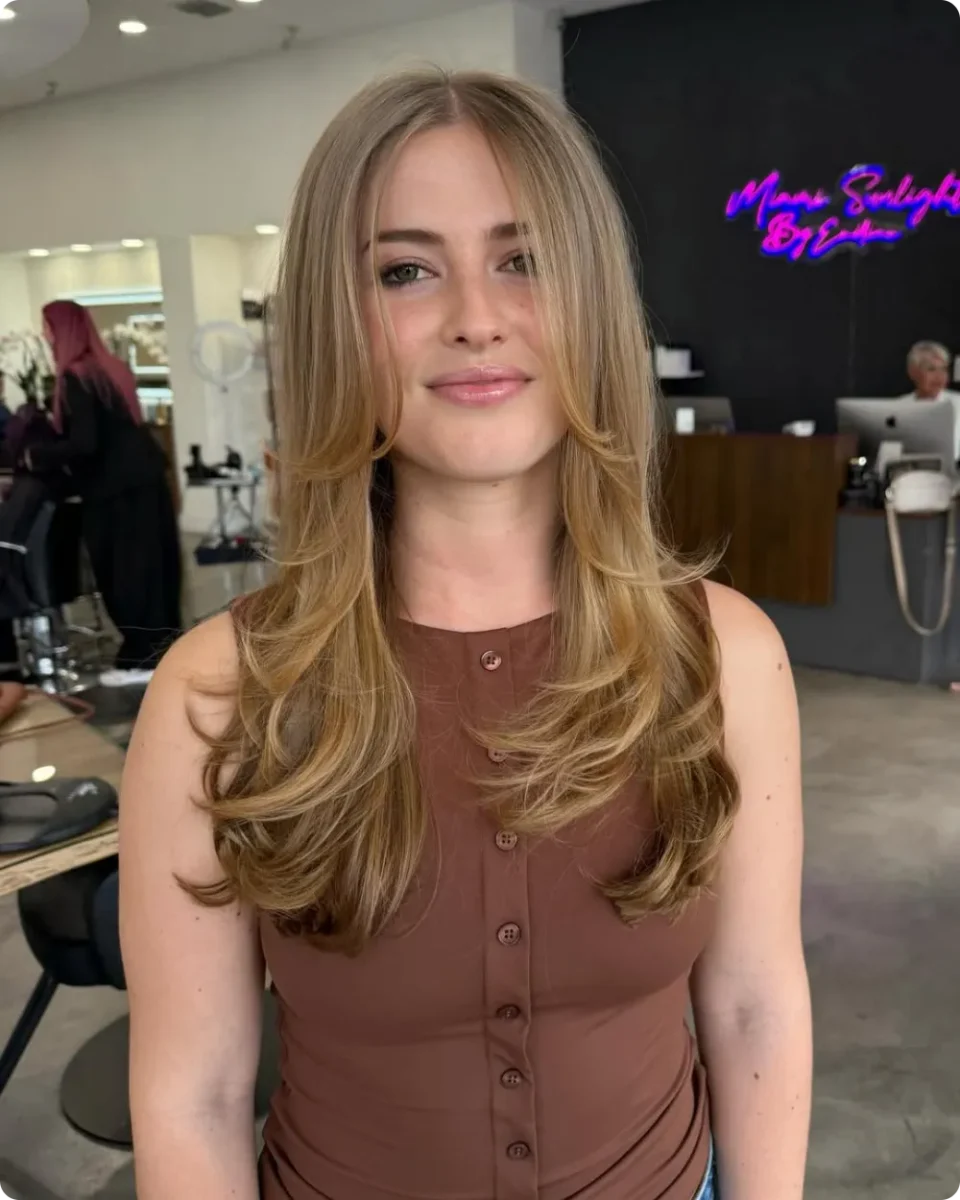 Feathered blonde layers with wispy pieces falling loose across the cheek