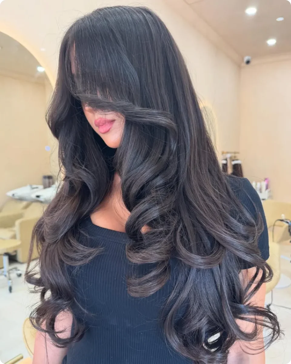 Long bangs and wide barrel waves on dense black hair falling past the chest