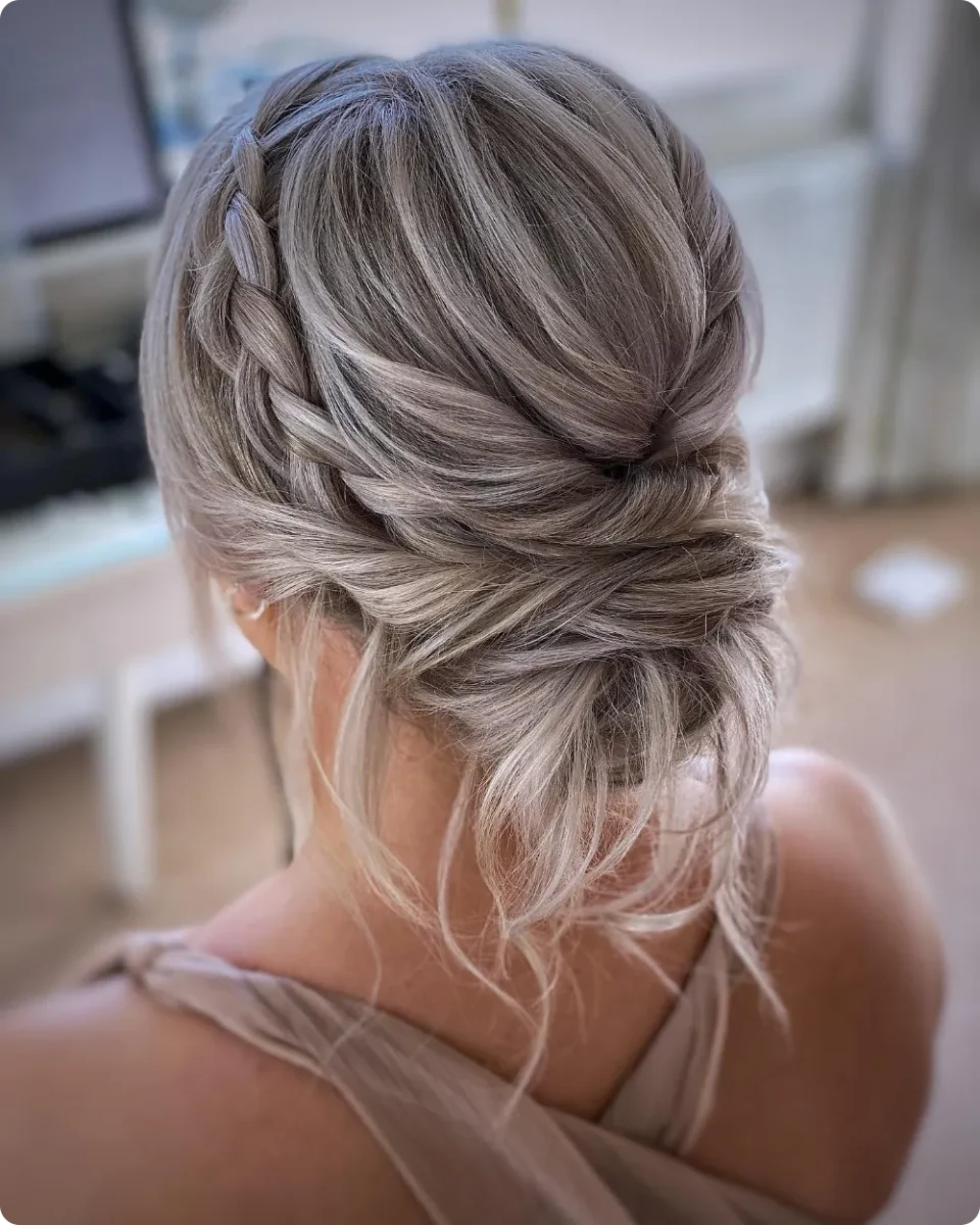 Braided halo updo on ash blonde long hair, with a side braid leading into a loose low bun and soft strands at the neck