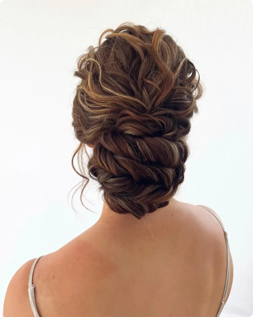 Wide curly twisted updo on brunette hair with caramel highlights, full volume at the crown, and one loose curl