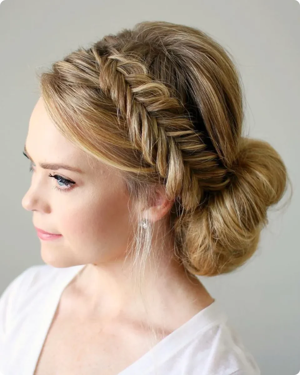 Fishtail crown braid on honey blonde hair leading into a loose low side bun, shown in side profile