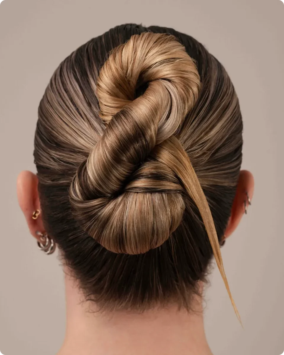 Glossy knotted bun on slicked back hair with caramel highlights, twisted into a sculpted knot with one loose strand