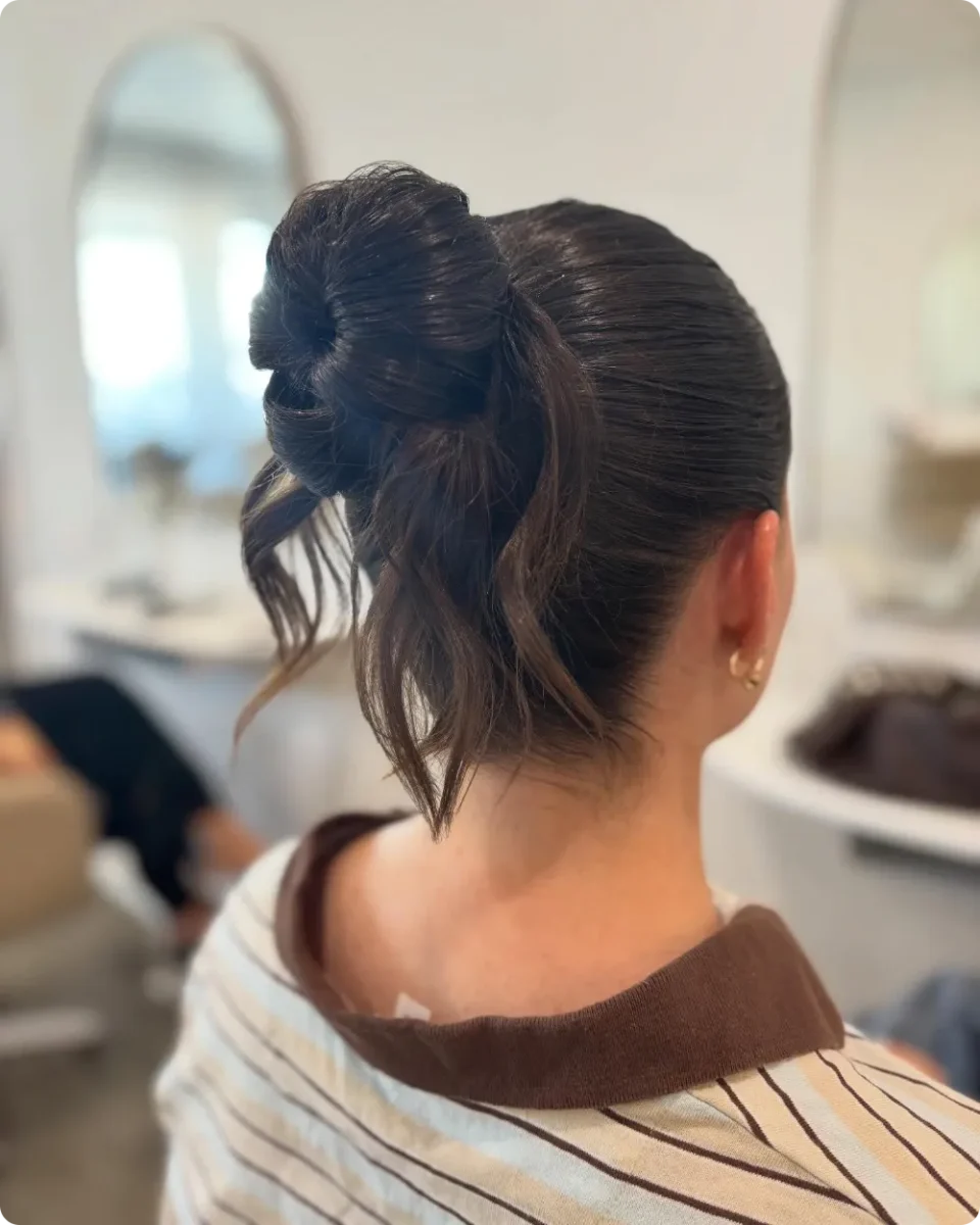Loose knot bun on dark brunette hair with slicked sides and waved ends left hanging below the knot
