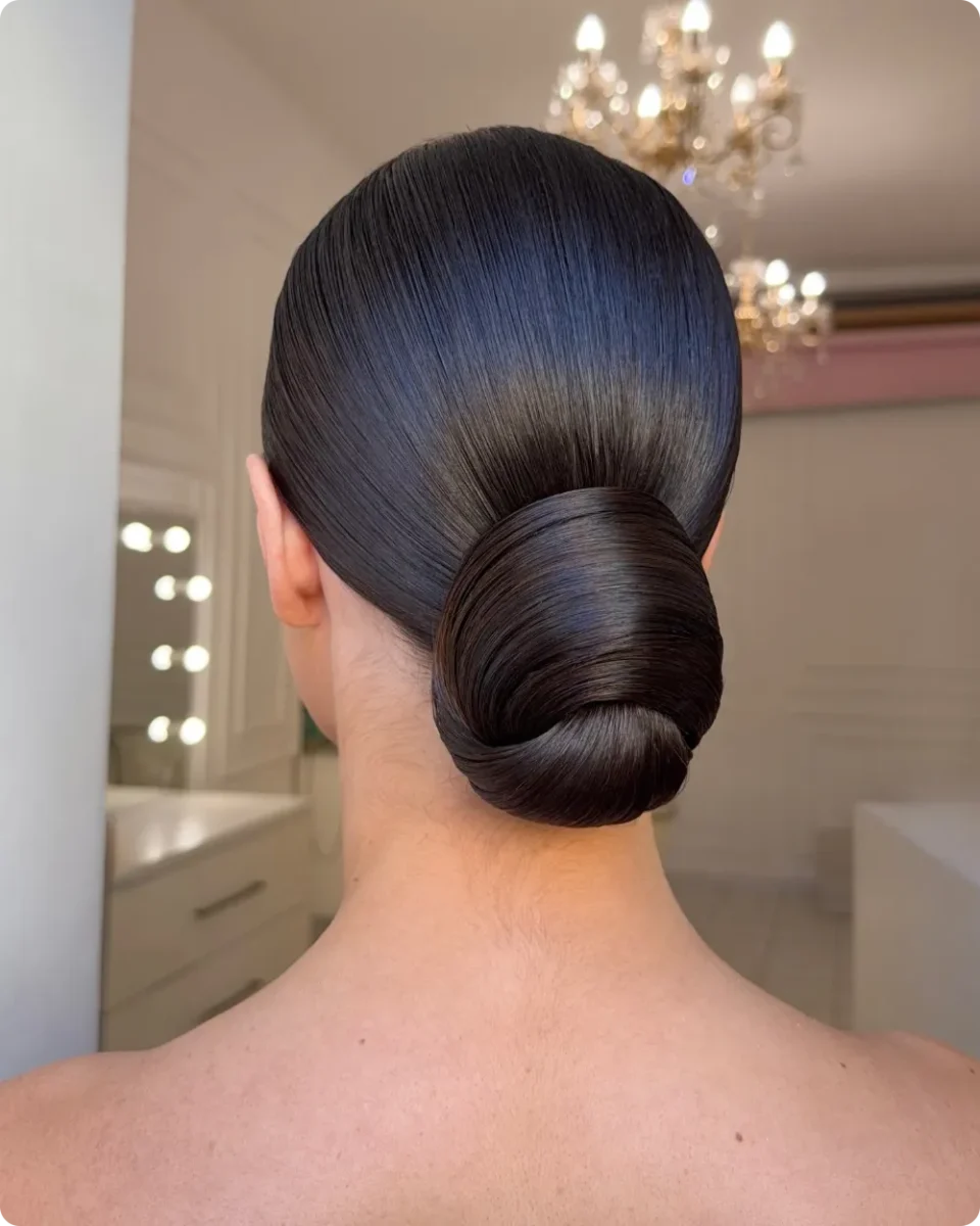 Mirror smooth chignon on jet black hair, swept back with no part and rolled into a wide low bun