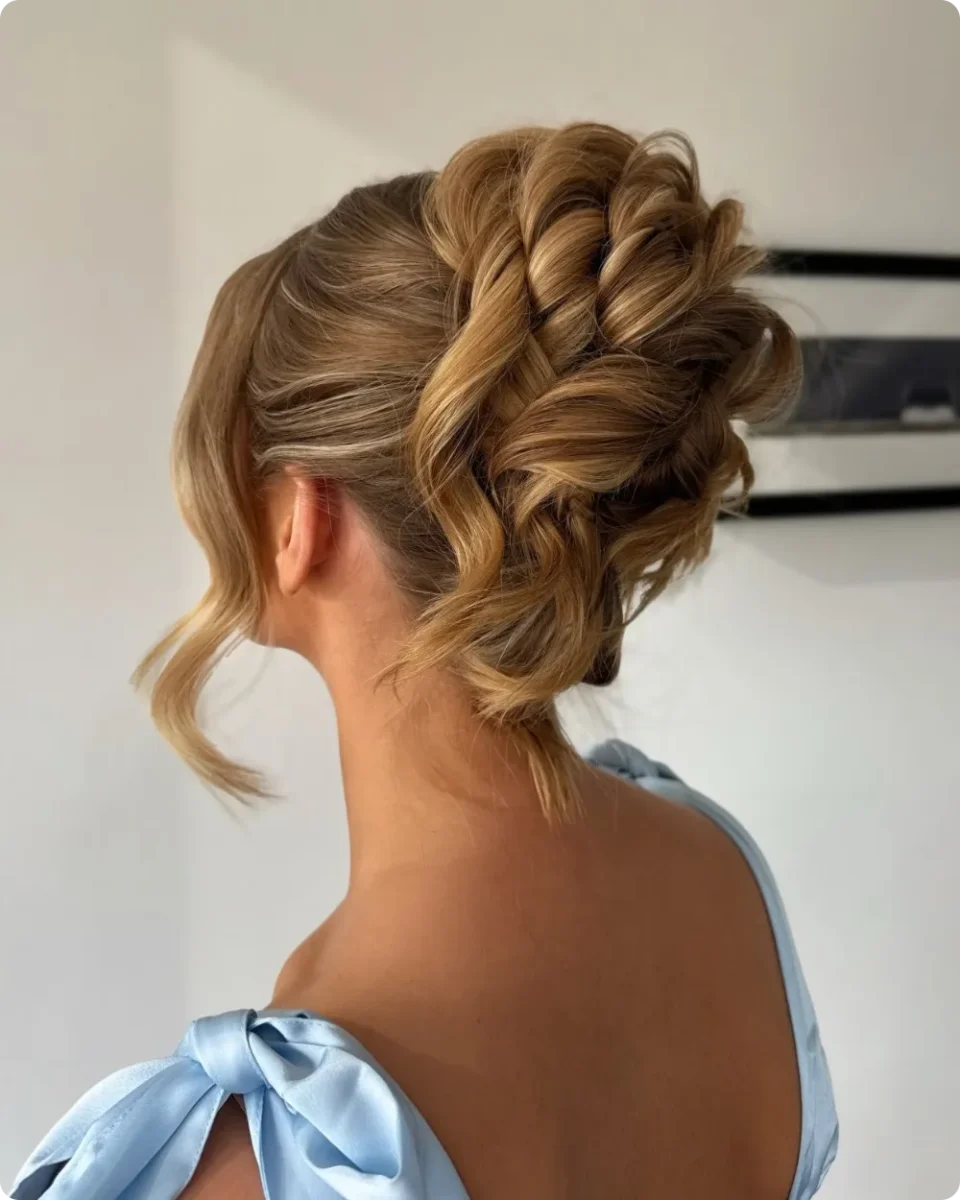 Rope braided updo on curled warm blonde hair, with chunky twists wrapped across the back and a soft wave by the ear