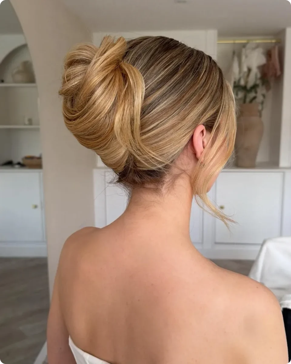 Textured high bun on honey blonde long hair with a loose folded knot and wispy strands, worn with a strapless top